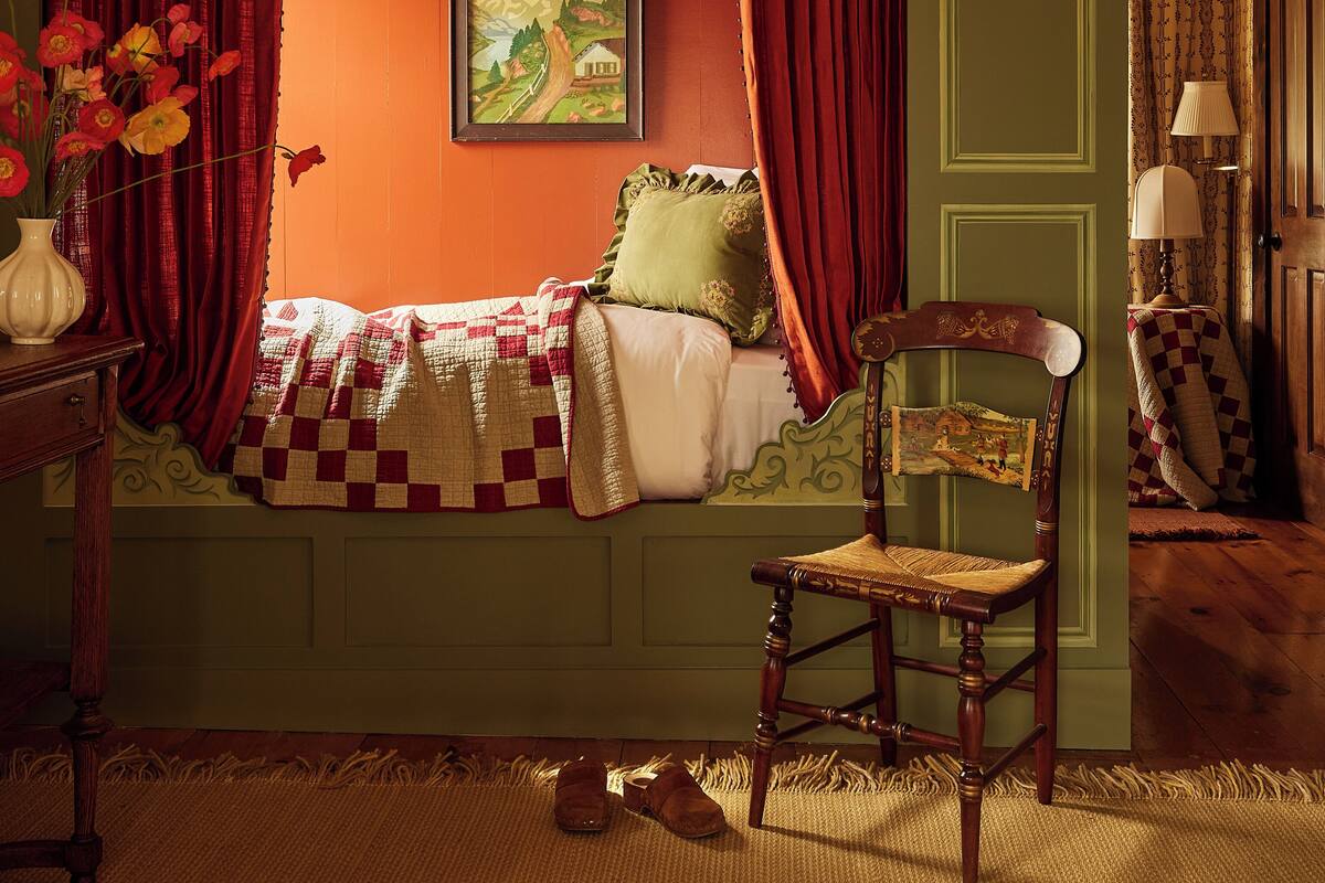 A room with a bed, a chair, a lamp, and a painting on the wall.