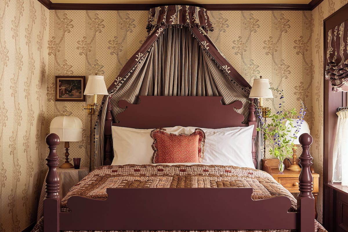 A traditional four-poster bed with a dark wooden frame, a quilted bedspread, and a matching bench.