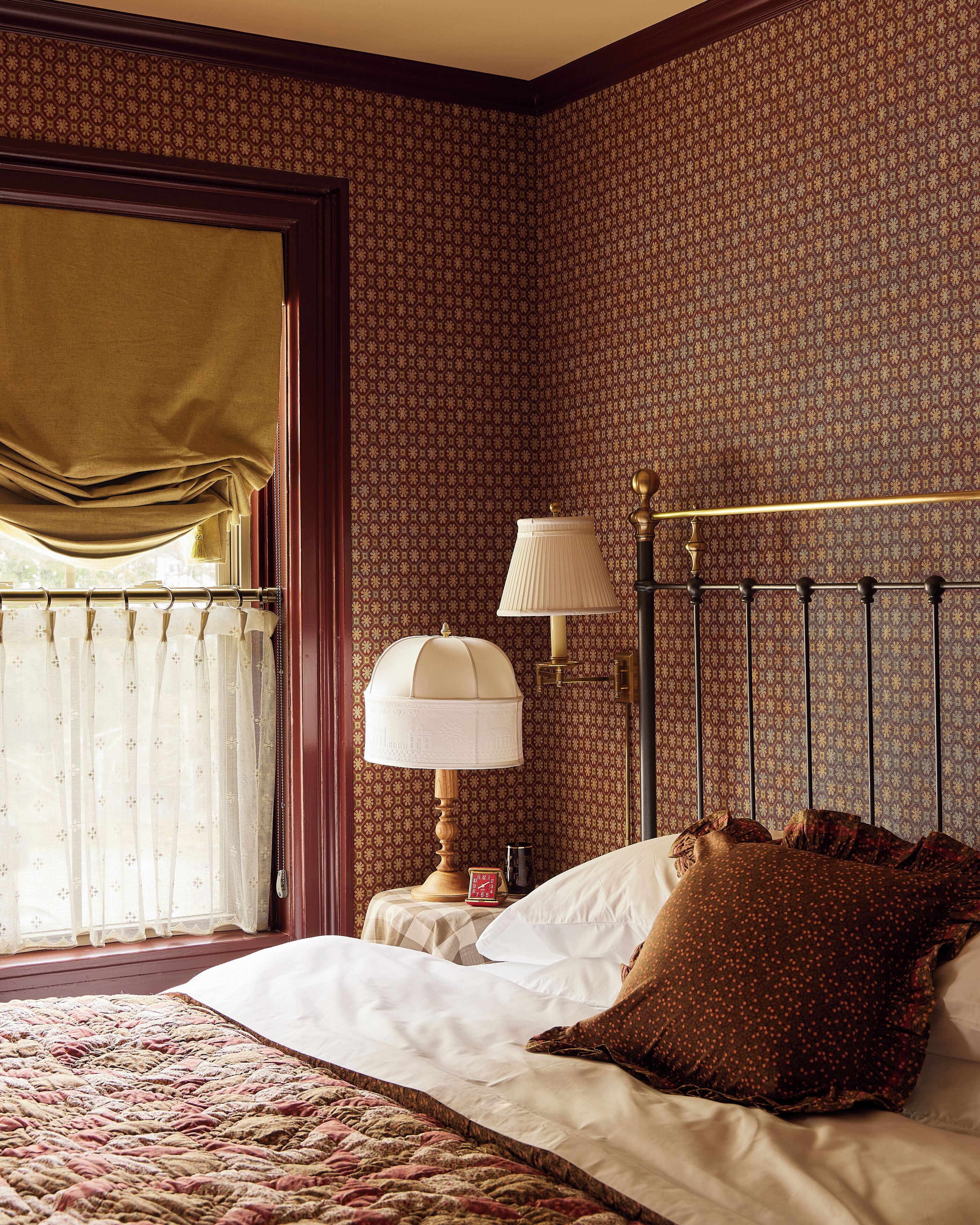 A neatly made bed with a patterned pillow, a bedside lamp, and a clock on a bedside table.