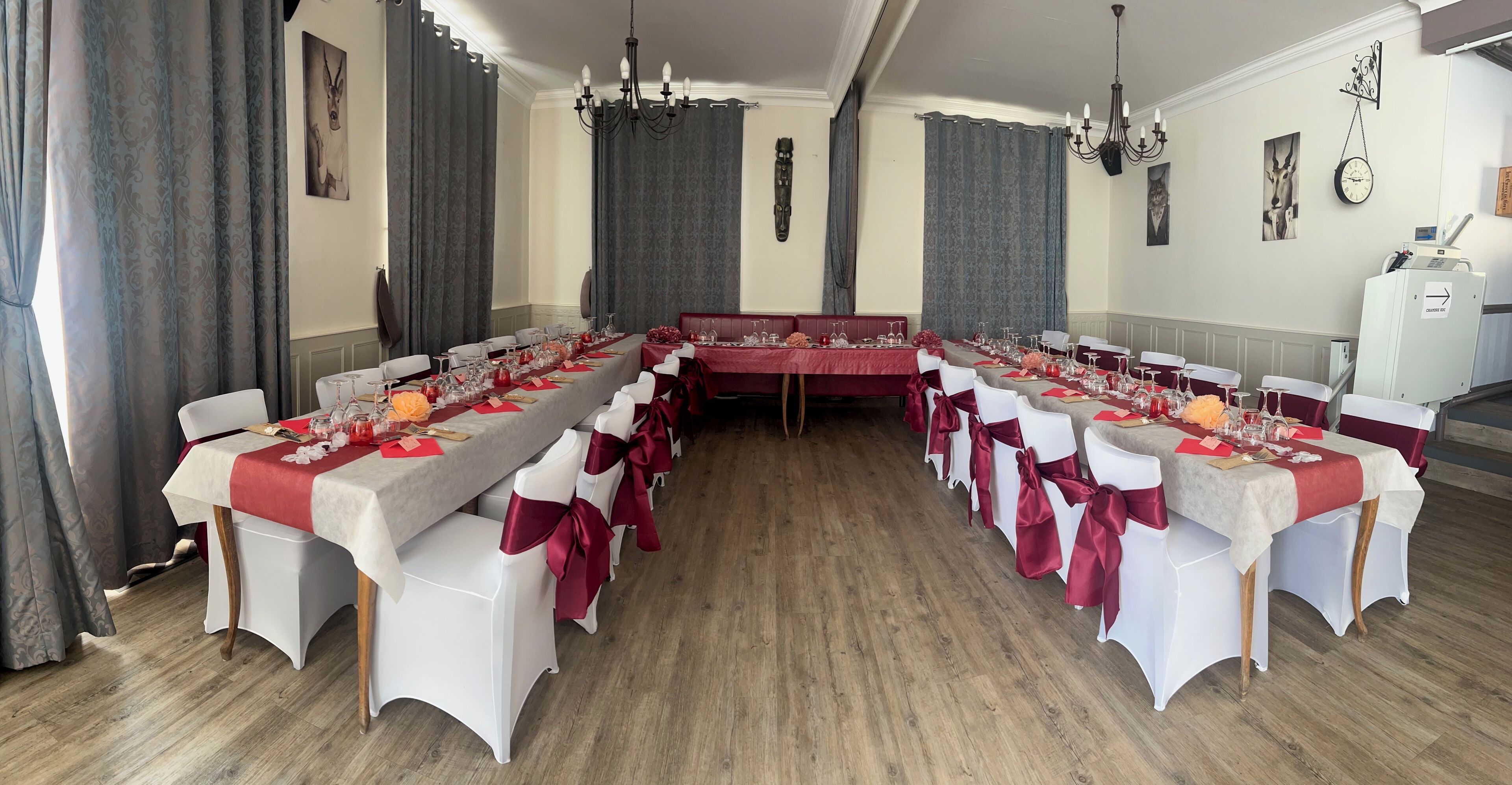A formal dining room with a long table set for a meal, white chairs with red sashes, and a red upholstered bench.