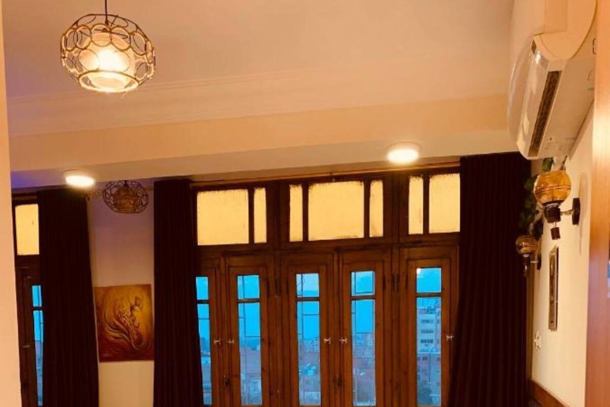Ett hotellrum med två sängar, ett stort fönster med gardiner, en krukväxt och en taklampa.