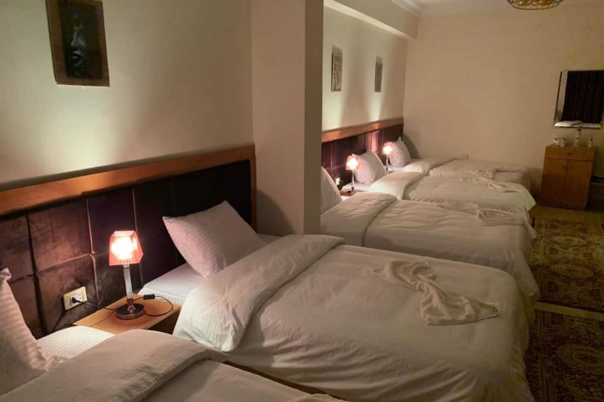 Ett hotellrum med fyra separata sängar, var och en med en sänggavel i trä och en sänglampa.