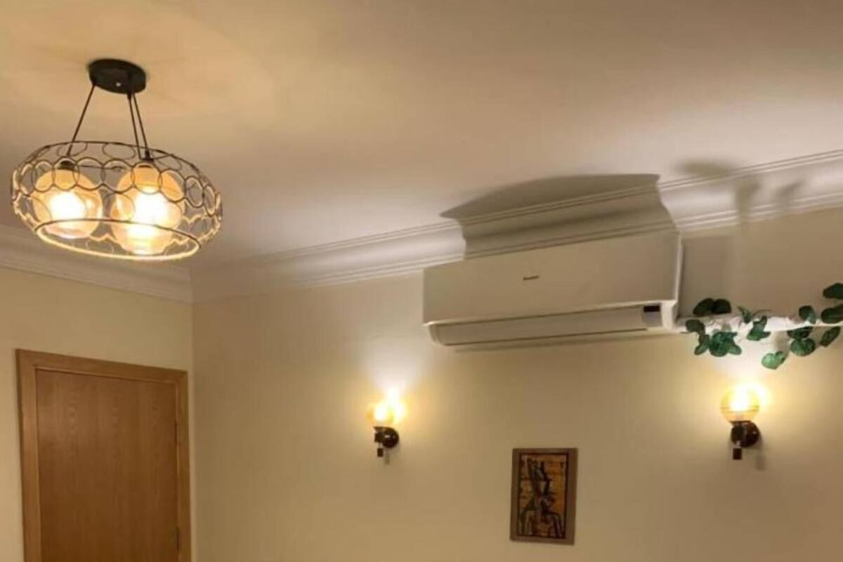 Ett hotellrum med två sängar, en sänggavel i trä, en luftkonditioneringsanläggning och väggmonterade lampor.