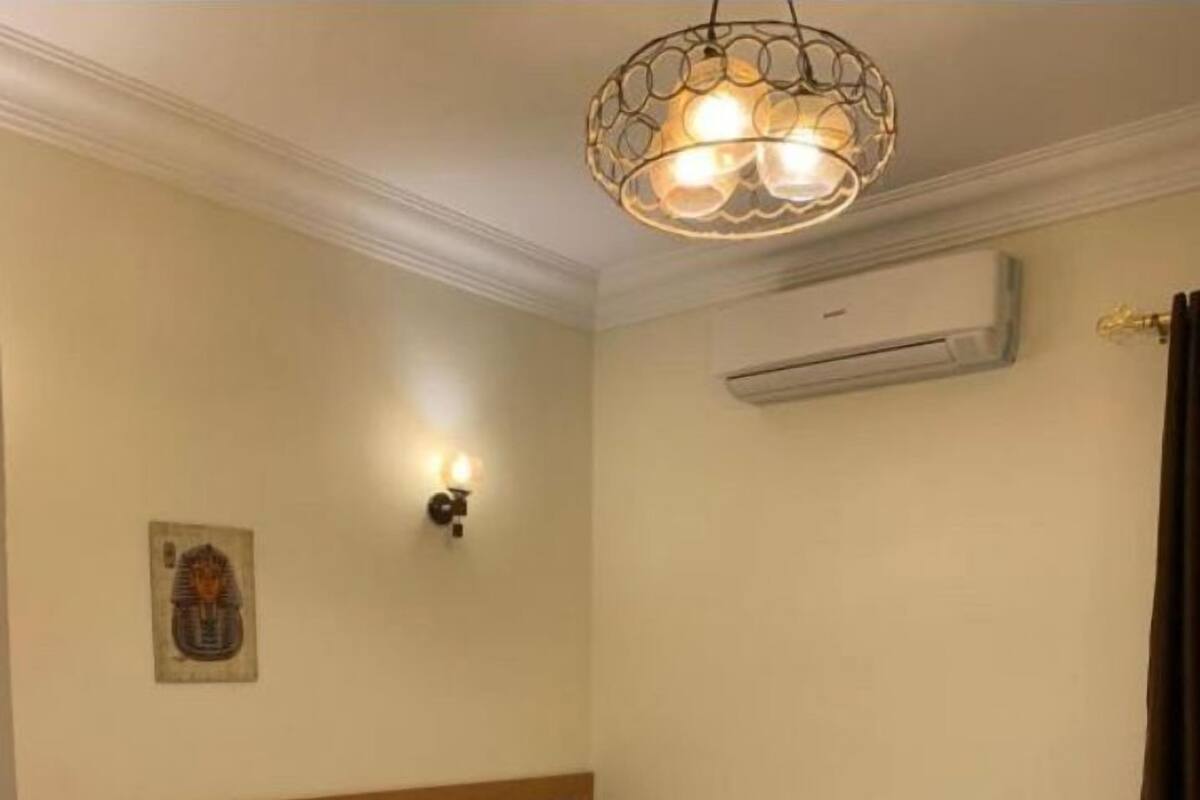 Ett hotellrum med två separata sängar, en sänggavel i trä, en väggmonterad luftkonditioneringsanläggning och en dekorativ lampa.