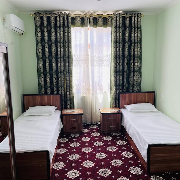 Una habitación con dos camas individuales, cabecera de madera, alfombra estampada y ventana con cortinas.