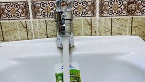 Ein Waschbecken mit fließendem Wasserhahn und einer Seifenspenderflasche.