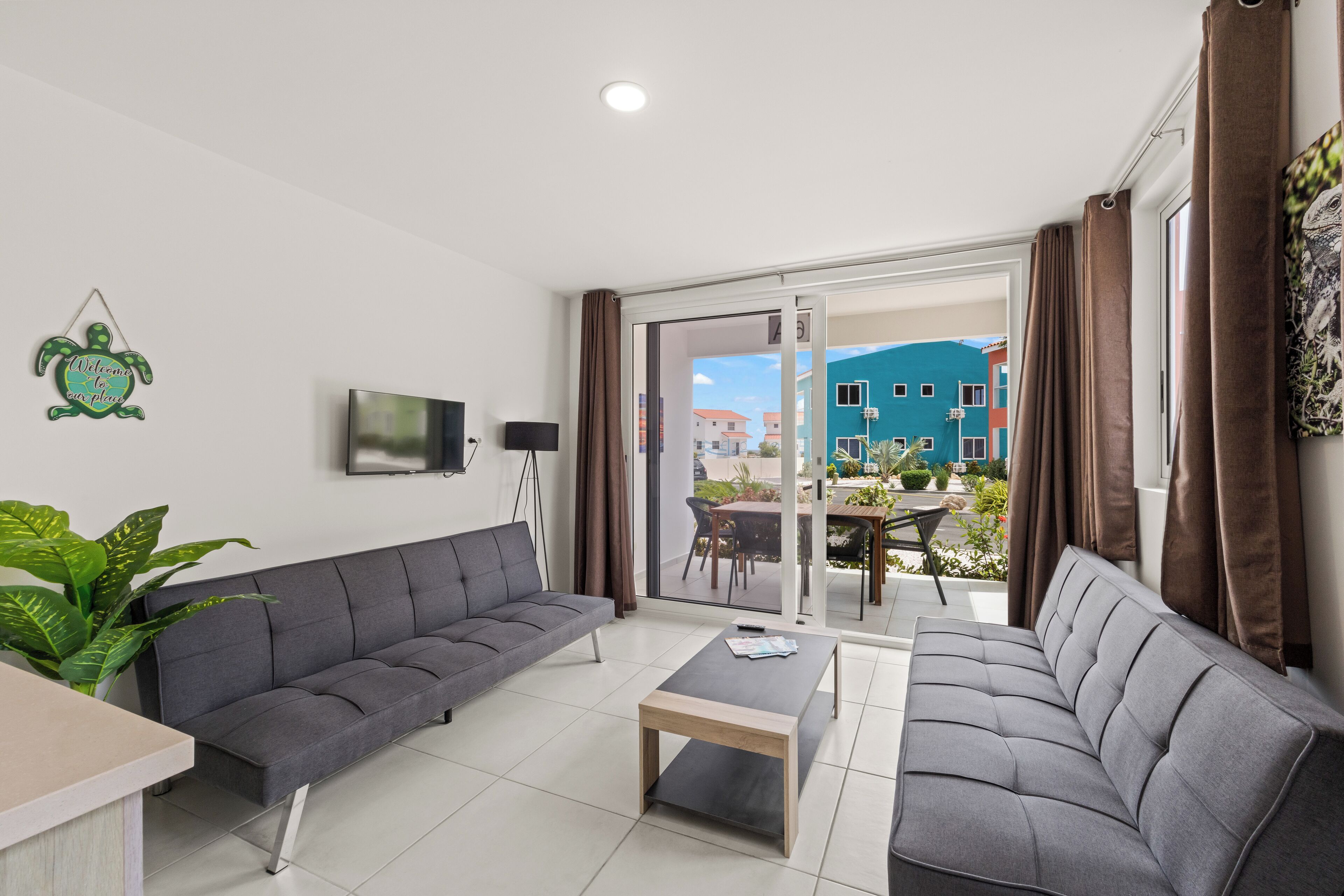 Een moderne woonkamer met een grijze bank, een houten salontafel en een flatscreen televisie aan de muur.