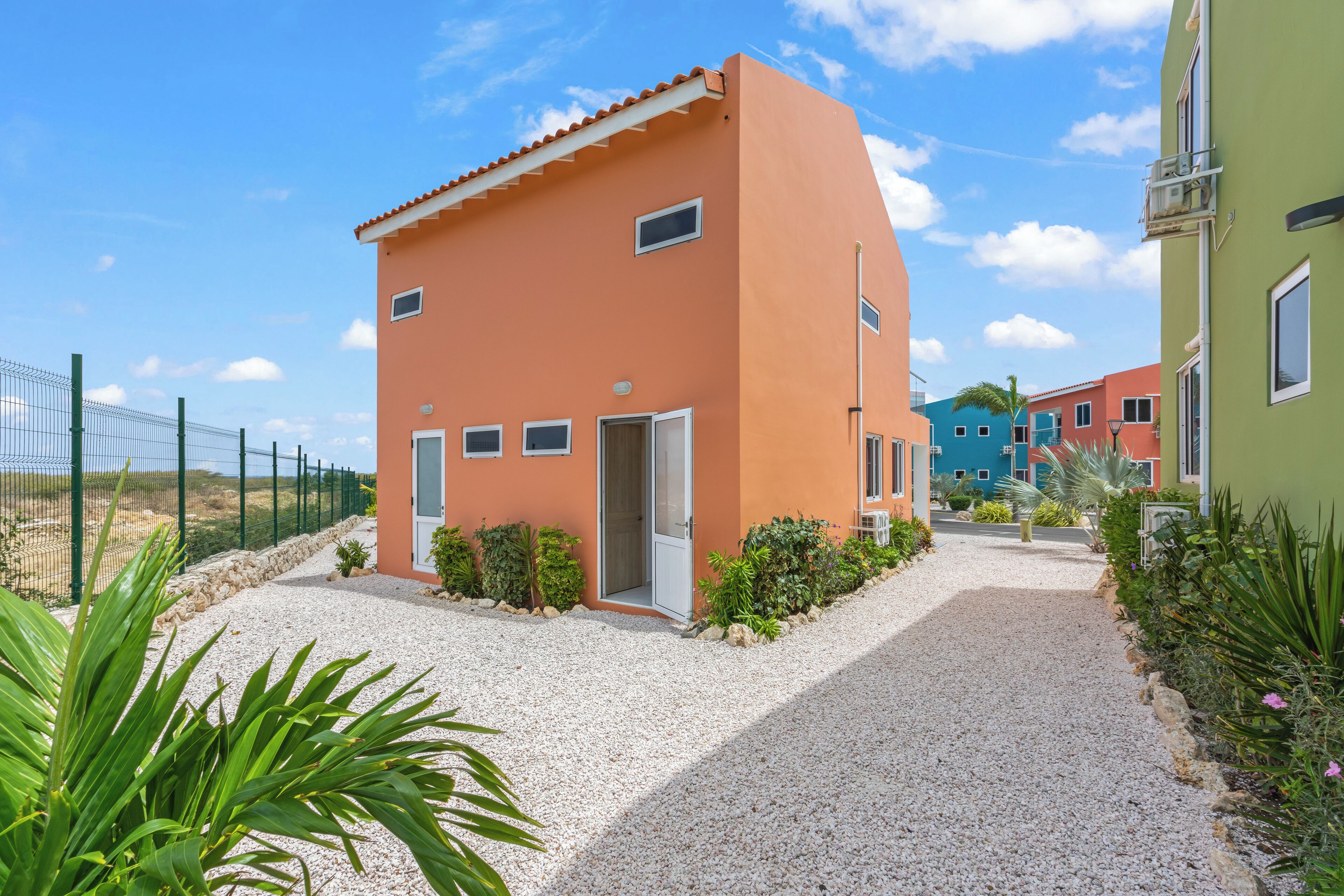 Un piccolo edificio a un piano con vialetto sterrato e recinzione in metallo.