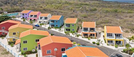 A coastal residential area with colorful houses, a road, and a view of the sea and mountains.