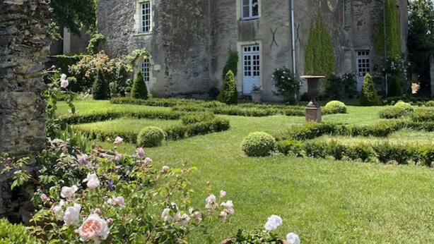Un edificio de piedra con una torre y un jardín bien cuidado con rosas.
