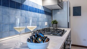 A modern kitchen with blue tiles, a gas stove, a bowl of mussels, and two glasses of white wine. - Velvet Stay | Ravizza 41 by Pleiades Home (Livorno)