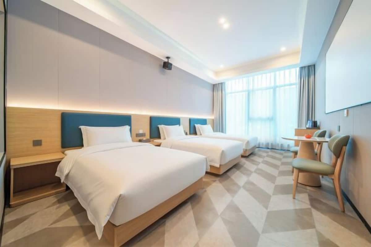 A hotel room with two beds, a desk, a chair, and a large window.