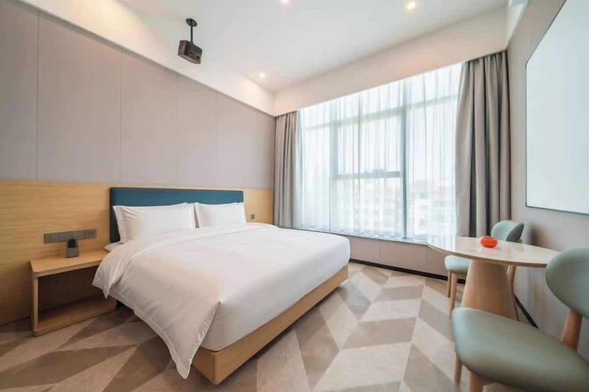 A hotel room with a bed, bedside table, chair, and a window with curtains.