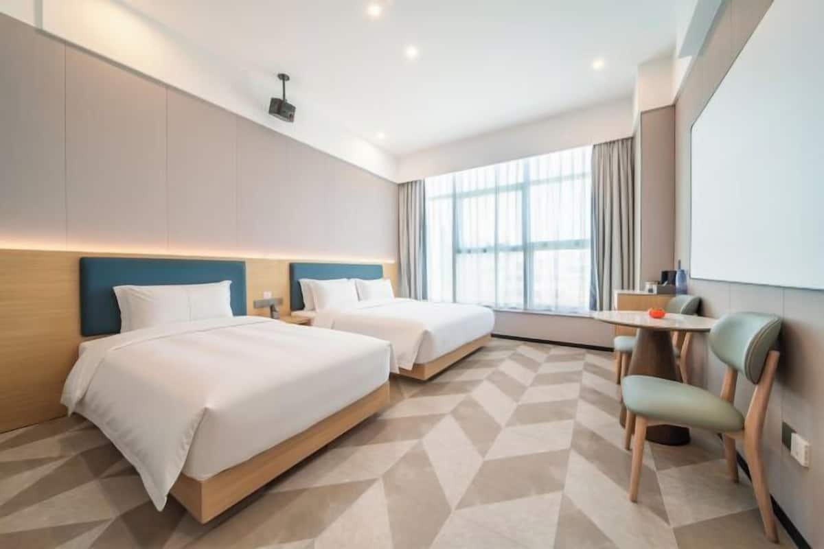 A hotel room with two beds, a desk, a chair, and a large window.