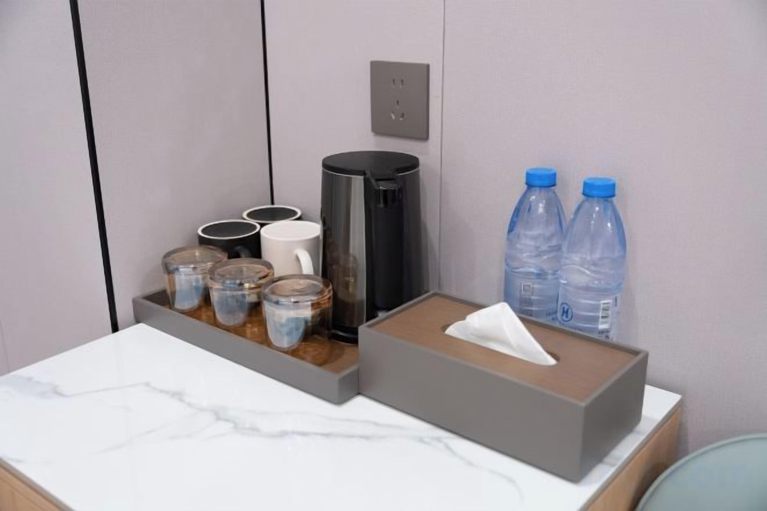A hotel room with a marble countertop, a coffee maker, a tissue box, and water bottles.