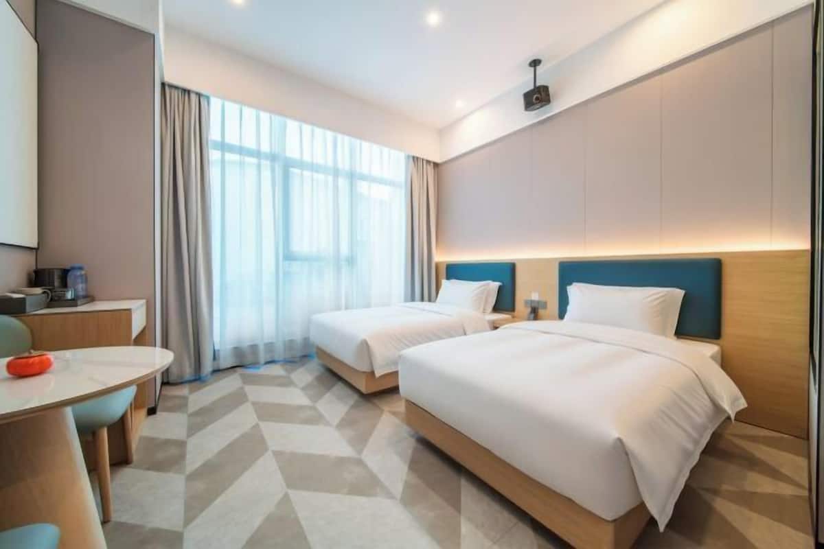 A hotel room with two beds, a desk, and a large window with curtains.