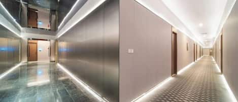 A modern hotel corridor with a reflective floor, a central elevator, and a patterned carpet.