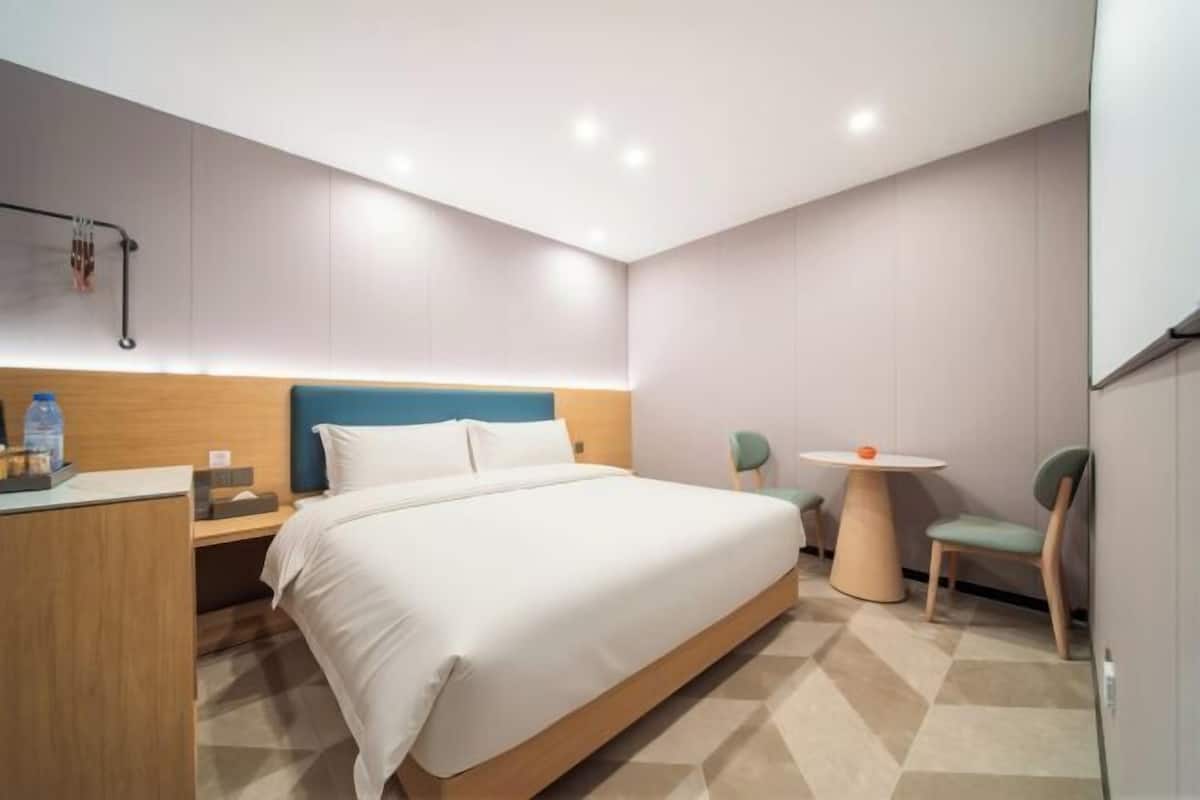 A modern hotel room with a large bed, bedside table, and a small round table with chairs.
