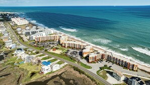 Vista aérea de un hotel costero con varias edificaciones, una playa y un puerto deportivo.