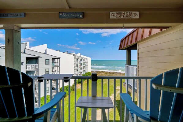 A balcony with a view of the ocean, a sign reading "Welcome to our Sandy Paradise," and a sign indicating "North Topsail Beach." - Beachfront Condo | Pool, Elevator, Park, Deck + Ocean & Sound Views (North Topsail Beach)