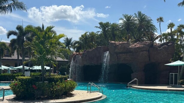 Piscina con cascada, rodeada de palmeras y un cielo despejado.