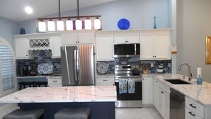 Una cocina moderna con gabinetes blancos, electrodomésticos de acero inoxidable, una isla de mármol e iluminación colgante.