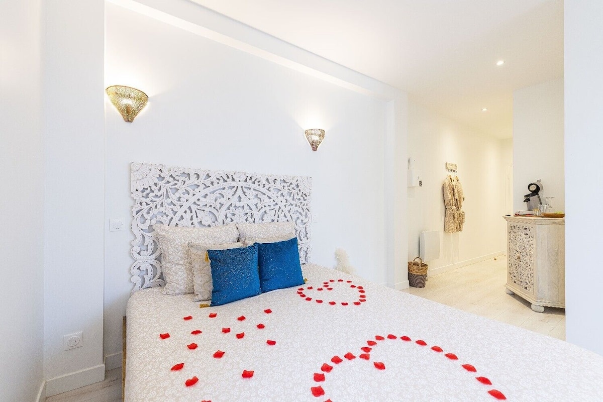 A bedroom with a patterned headboard, a bed with blue and white bedding, and a decorative arrangement of red rose petals on the floor.
