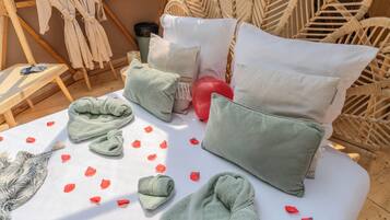 A room with a bed, pillows, a blanket, a towel, and scattered rose petals.