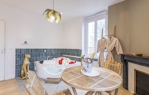 Une salle de bain moderne avec une baignoire, une statue de chat dorée, un luminaire décoratif et une table sur laquelle se trouve une bouteille de champagne.