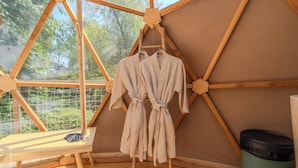 Habitación de madera con vista a zonas verdes, un banco y dos batas colgadas en un perchero.