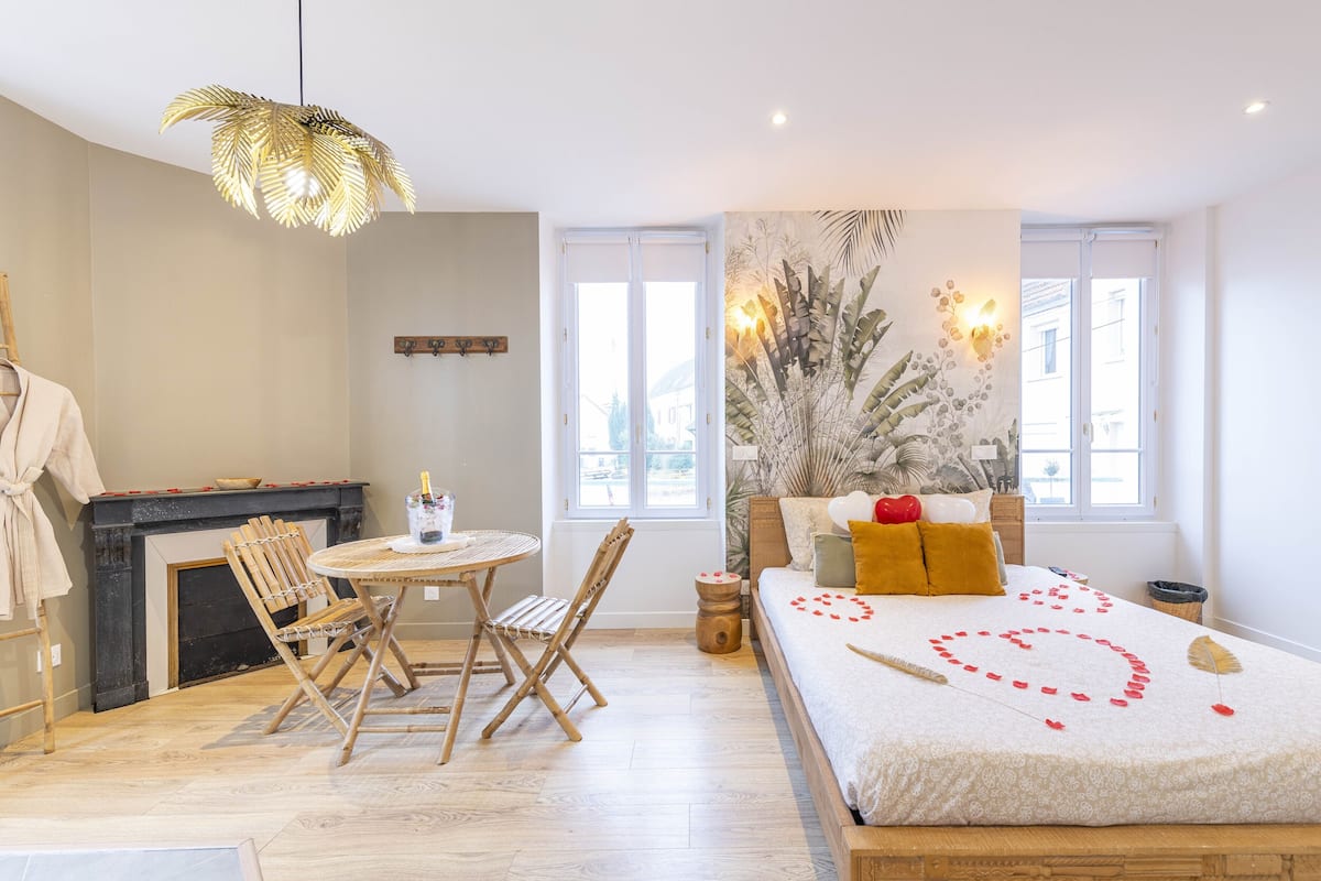 A bedroom with a bed, a fireplace, a dining table, and a large window.