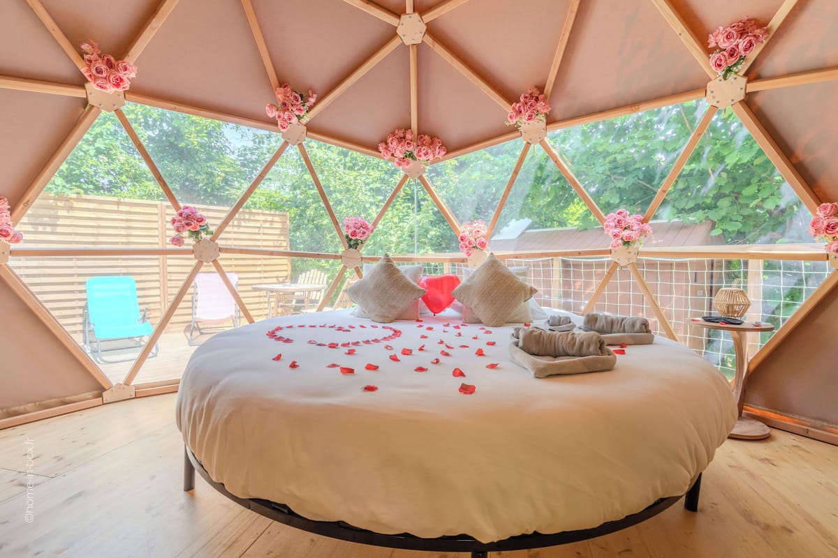 A bedroom with a bed, pillows, and a view through a geometric window.