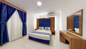 Een hotelkamer met een groot bed, een houten dressoir, een spiegel en een raam met blauwe gordijnen.