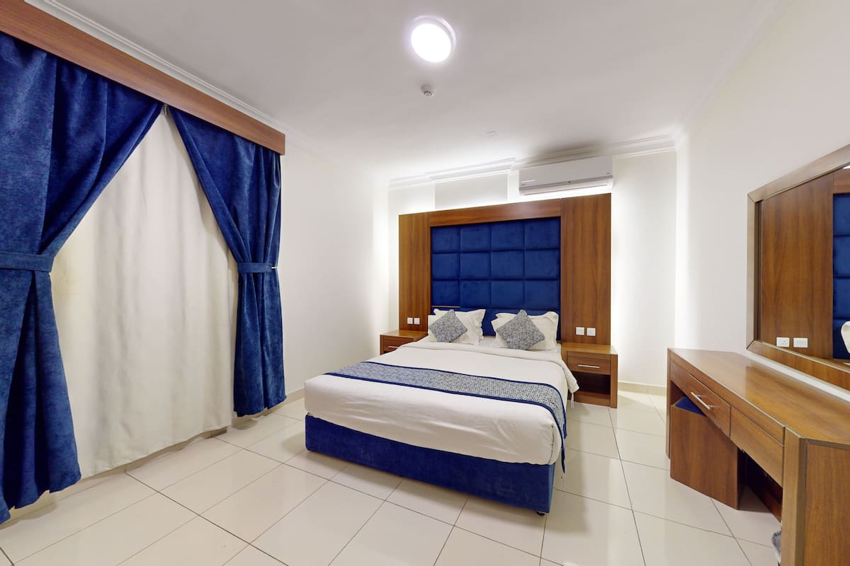 A hotel room with a large bed, a wooden dresser, a mirror, and a window with blue curtains.
