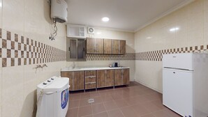 Een kleine keuken met een wasmachine, een koelkast en houten kastjes.