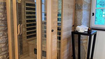 A sauna with glass doors, wooden panels, and a stone wall backdrop.