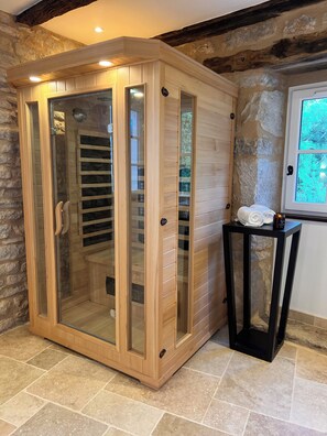 A sauna with glass doors, wooden panels, and a stone wall backdrop. - Noubar  (Cénevières)