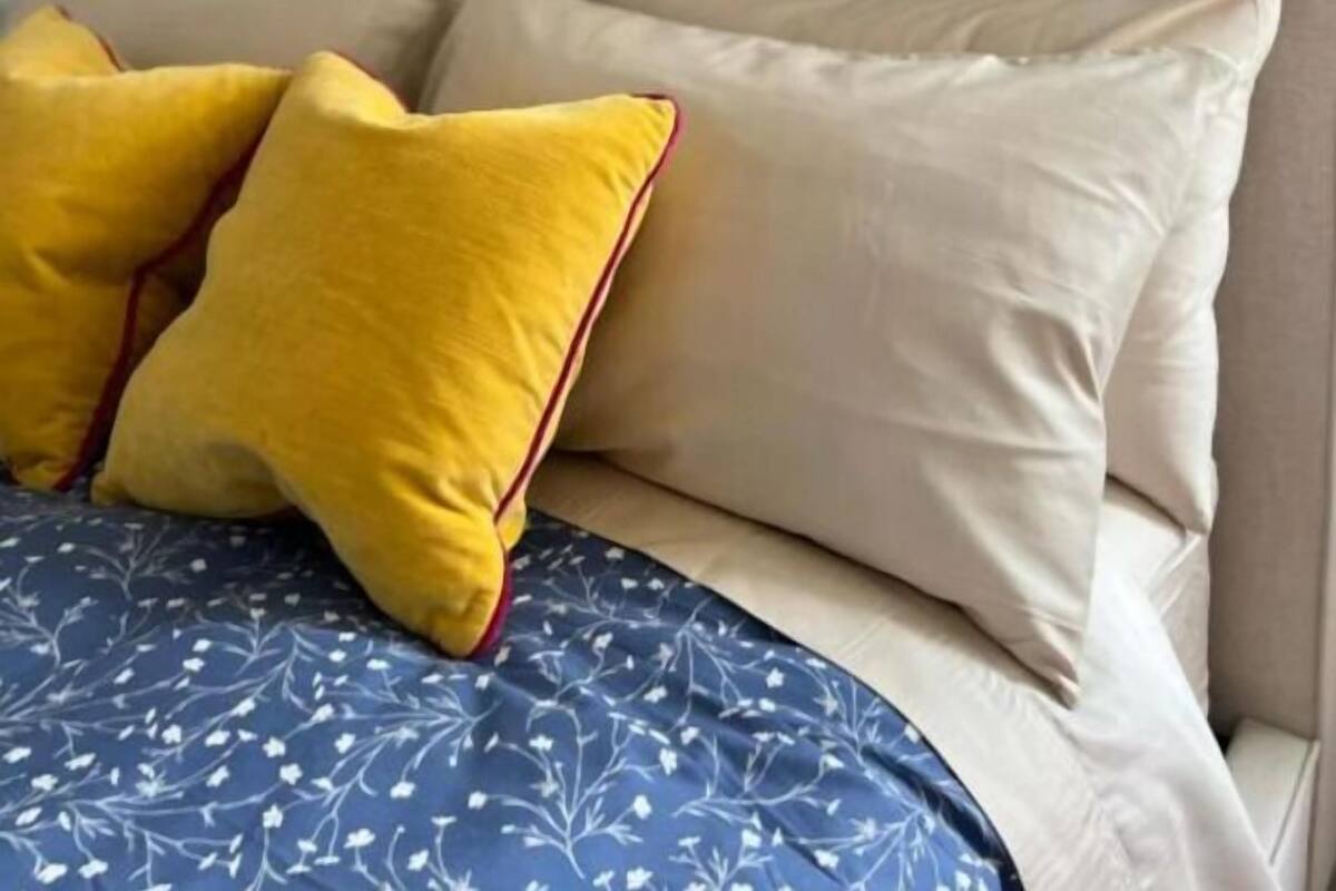 A bed with a blue floral bedspread, two yellow pillows, and a beige headboard.