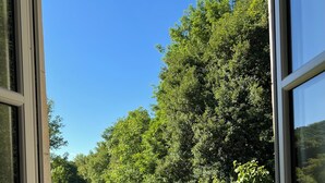 A window view of a green field and trees, with a clear blue sky. - Noubar  (Cénevières)