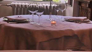 A dining table set for two with wine glasses and a candle, positioned near a window with a view of a garden. - Noubar  (Cénevières)