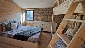 Une chambre dans une cabane en bois, avec un lit superposé, une commode et une fenêtre donnant sur un mur en pierre.