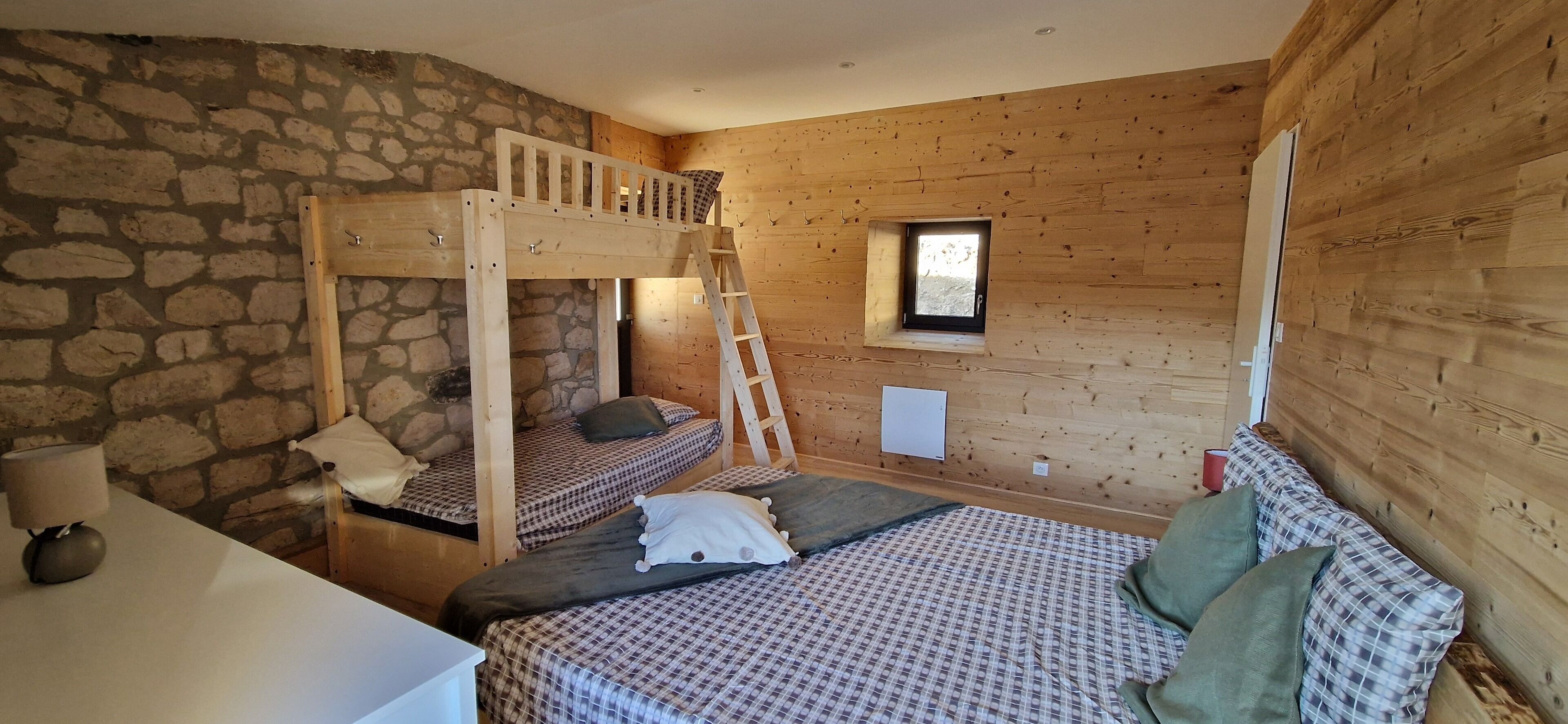 Un dormitorio con literas, una pared de madera, una pared de piedra, una ventana y una mesita de noche.