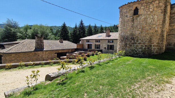 Un bâtiment en pierre doté d’une tour, entouré d’un jardin et bordé d’un chemin de terre.