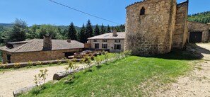 Un bâtiment en pierre doté d’une tour, entouré d’un jardin et bordé d’un chemin de terre.