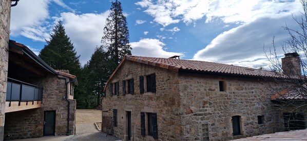 Un bâtiment en pierre avec un toit en tuiles, un balcon en bois et une allée gravillonnée.