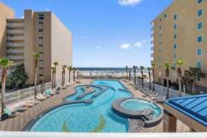 A hotel pool area with a view of the beach, palm trees, and a clear sky. - Ocean View Condo with Pools and Lazy River (Gulf Shores)