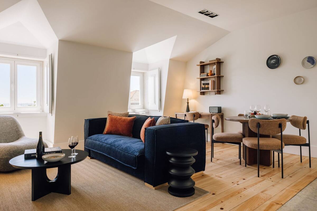 Ein modernes Wohnzimmer mit einem dunkelblauen Sofa, einem runden Couchtisch und einem Essbereich mit einem Holztisch und Stühlen.