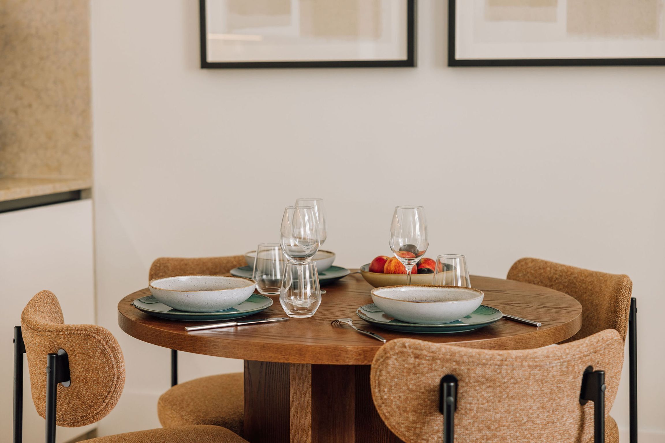 A round dining table with four chairs, clear glassware, and a bowl of fruit.