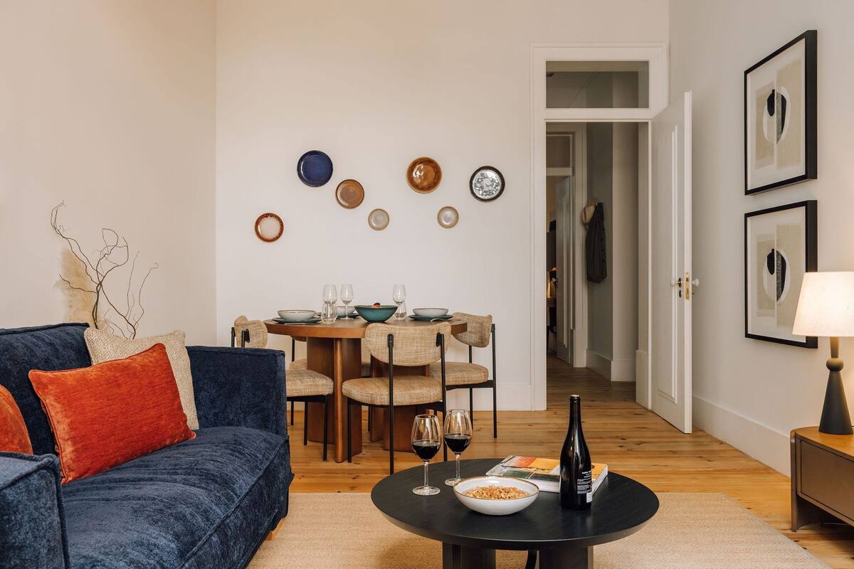 Ein Wohnzimmer mit blauem Sofa, einem Esstisch mit Stühlen und einem Couchtisch mit Flasche und Gläsern.
