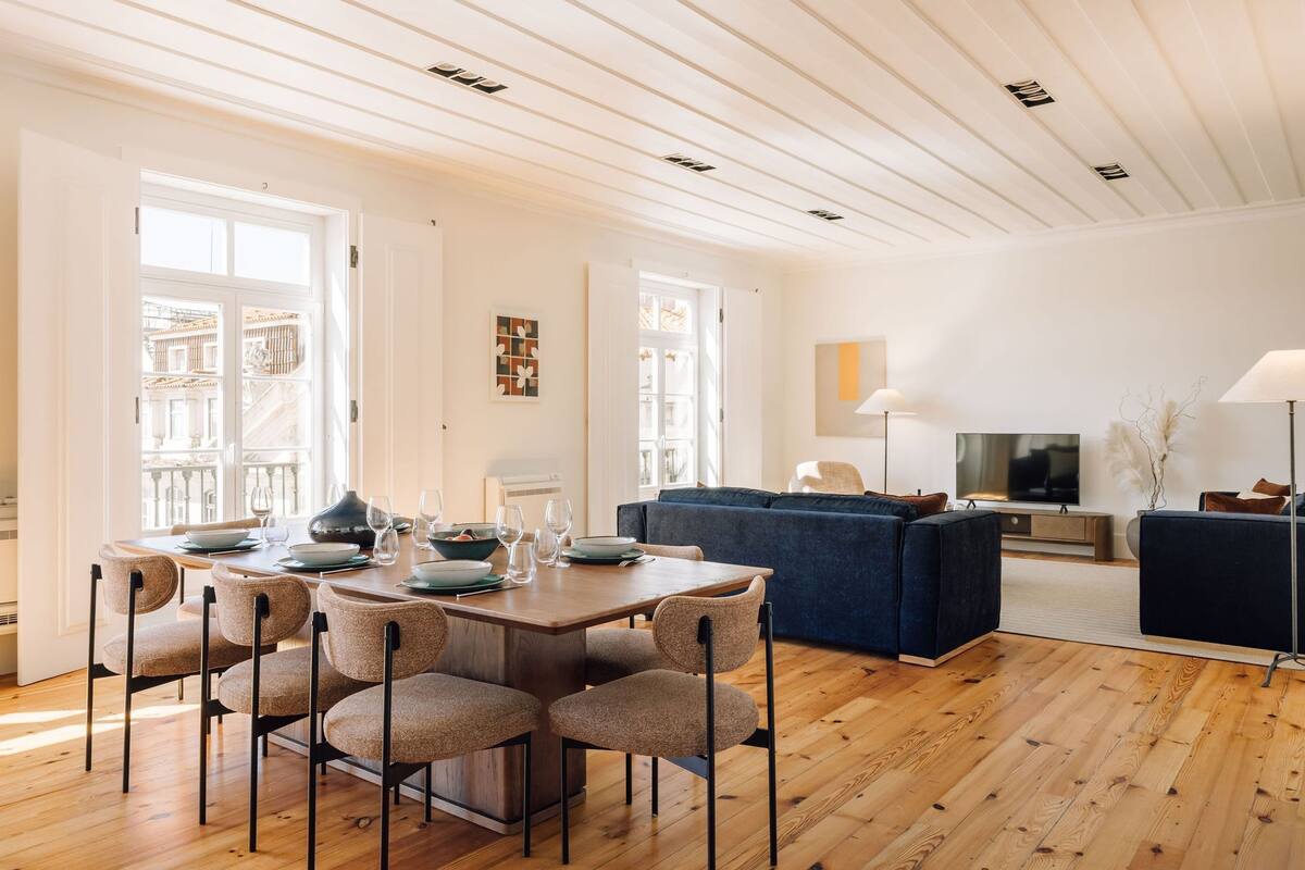 Ein geräumiger Wohnbereich mit Holzboden, einem Esstisch für vier Personen und einem dunkelblauen Sofa.